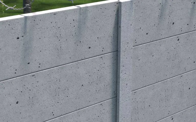Szare przemysłowe ogrodzenie betonowe z gładkimi płytami i drutem kolczastym nad nim
